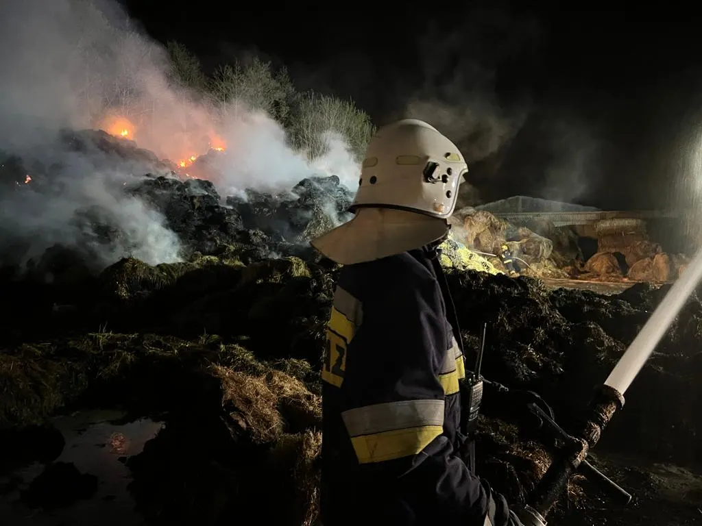 Strażak w hełmie i rękawicach podający wodę podczas nocnego gaszenia pożaru